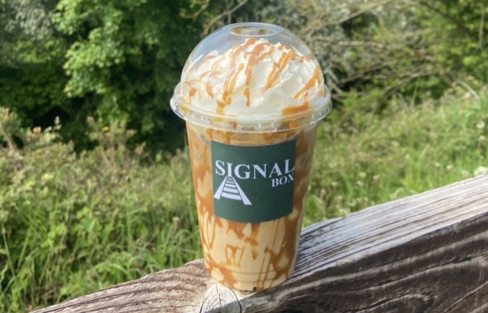 an iced coffee with a sticker that reads "Signal Box", greenery in the background