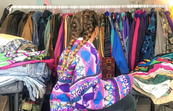 girl in colourful fleece sorting through a rack of vintage clothing