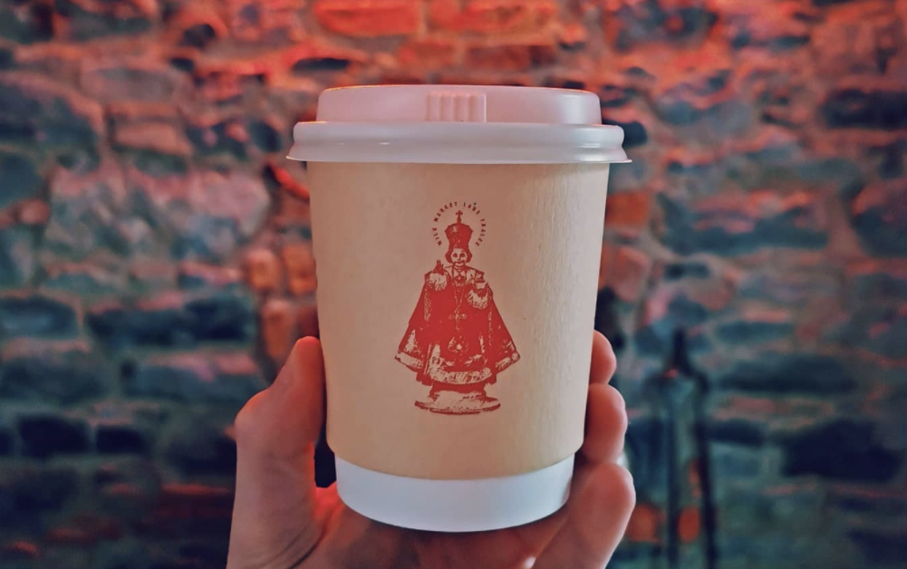 cream takeaway coffee cup with a red line illustration of the child of prague on the front