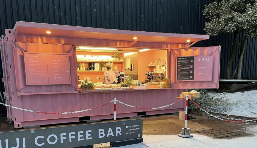 exterior of guji coffee bar, a converted shipping container painted pale pink with coffee equipment and treats display inside