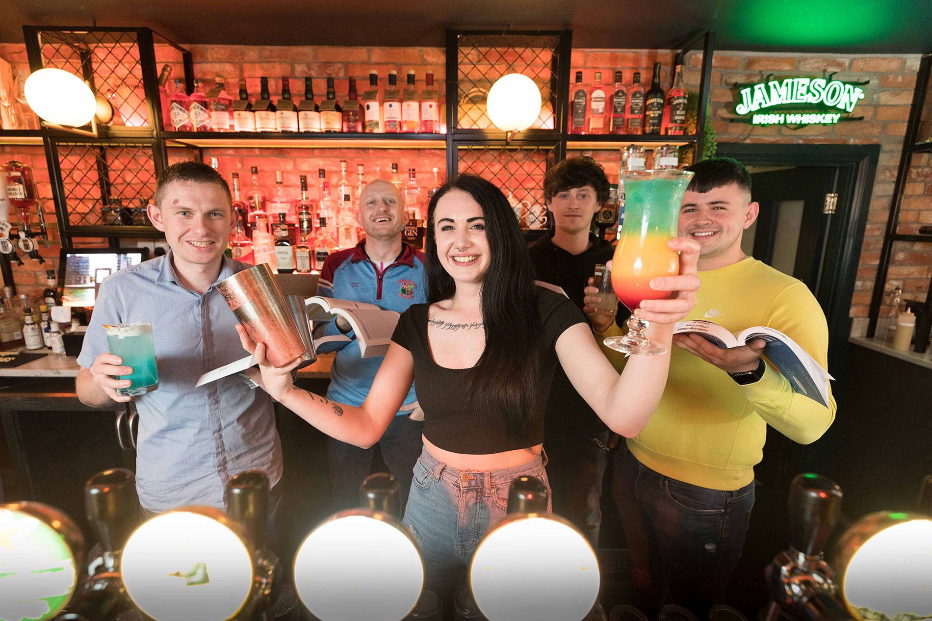people behind a bar shaking cocktail makers and holding drinks