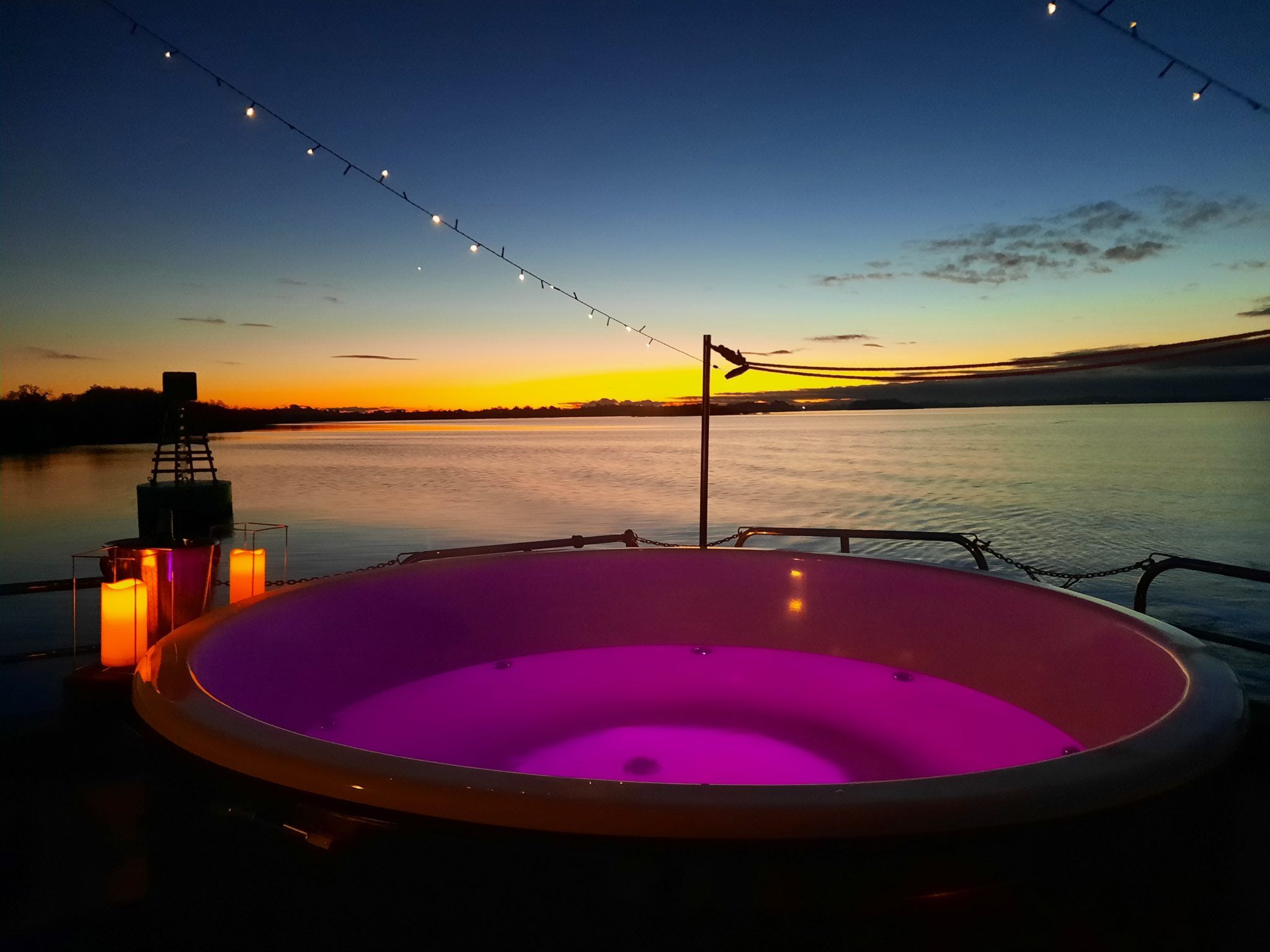 hot tub surrounded by fairy lights and lanterns, a body of water in the background