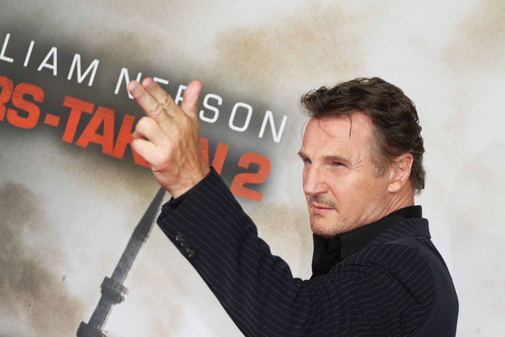 Liam Neeson pointing at camera with two fingers