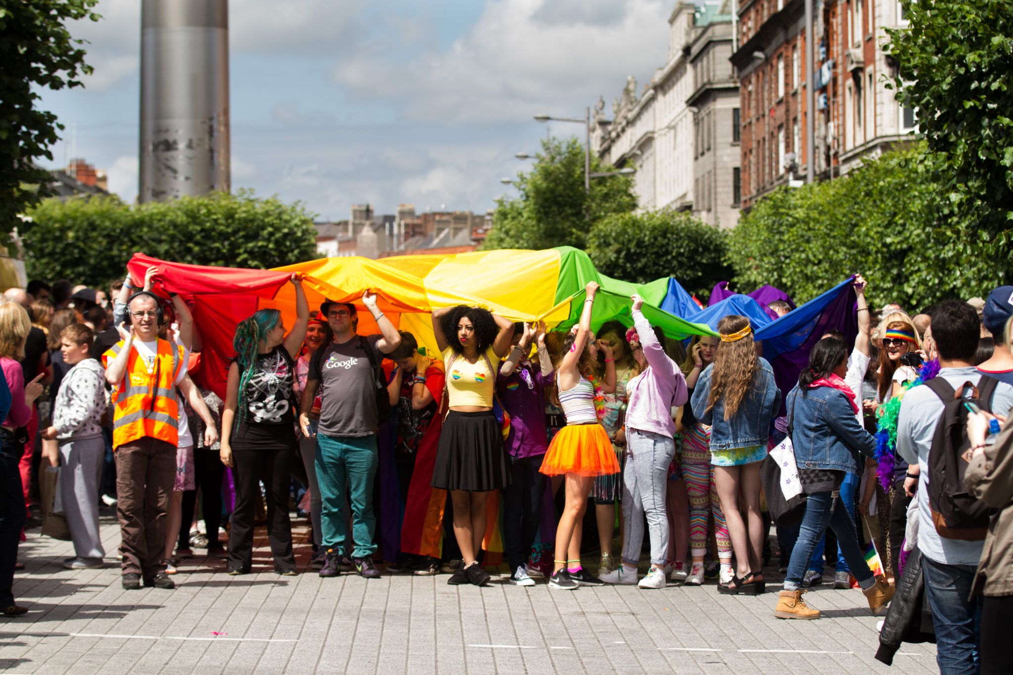 group of people on O'Connell Street holding a giant pride flag over their heads