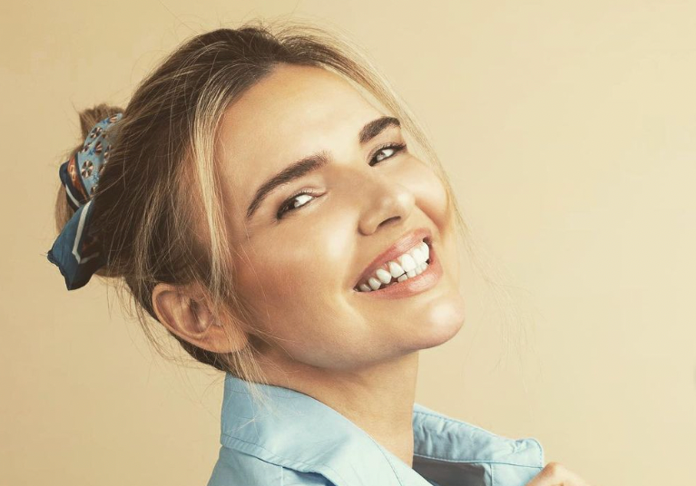 nadine coyle smiling at camera against a beige coloured background