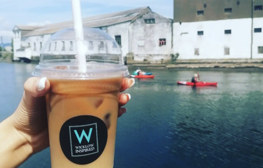 iced coffee cup being held out in front of a body of water with two people kayaking in the background