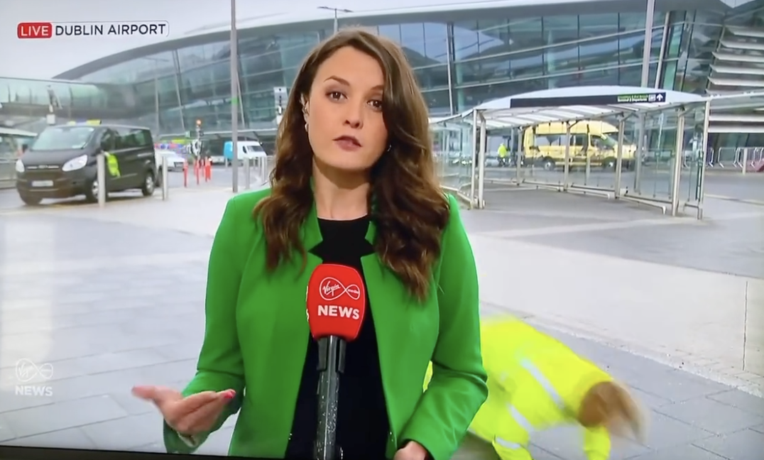 a newsreader speaking to camera at Dublin Airport with a man falling in the background