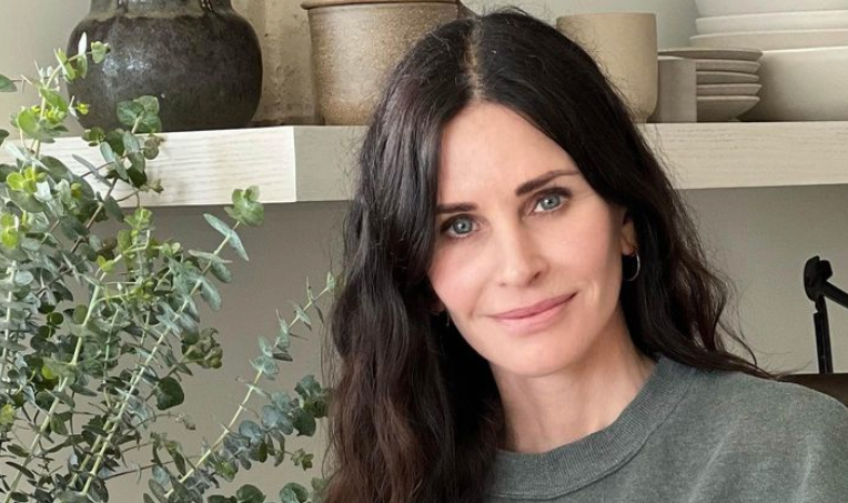 courteney cox looking at camera, wearing a green jumper