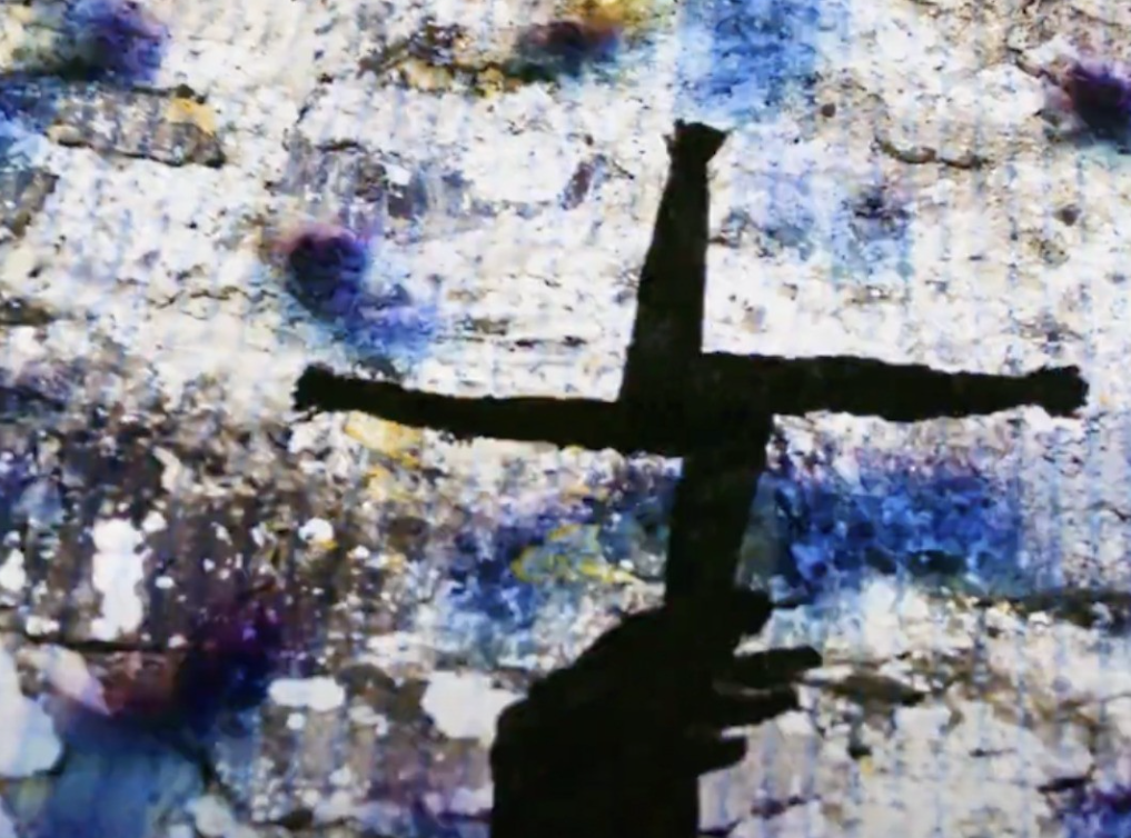 person holding a St Brigids cross made from rushes against a colourful abstract background